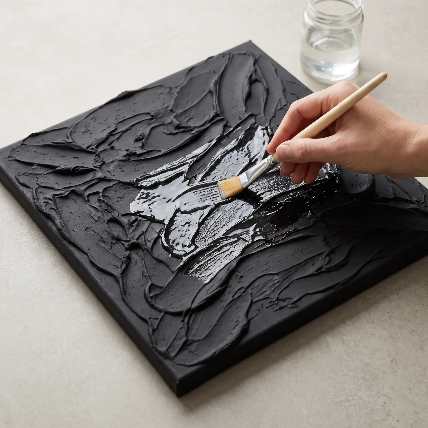Applying mixtion with a brush to a black textured relief on canvas
