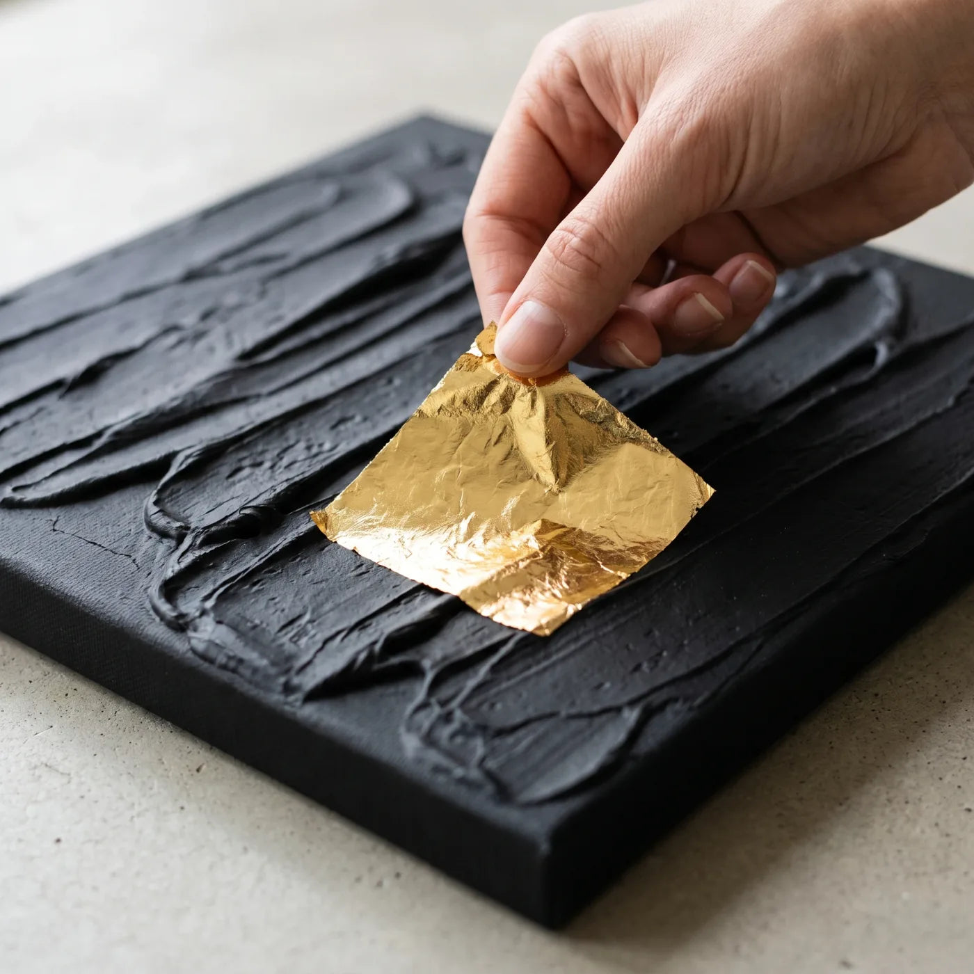 Applying a sheet of gold leaf to a black textured relief
